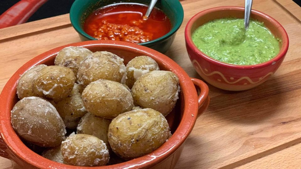 Papas sazonadas acompañadas de salsas roja y verde en recipientes de cerámica.