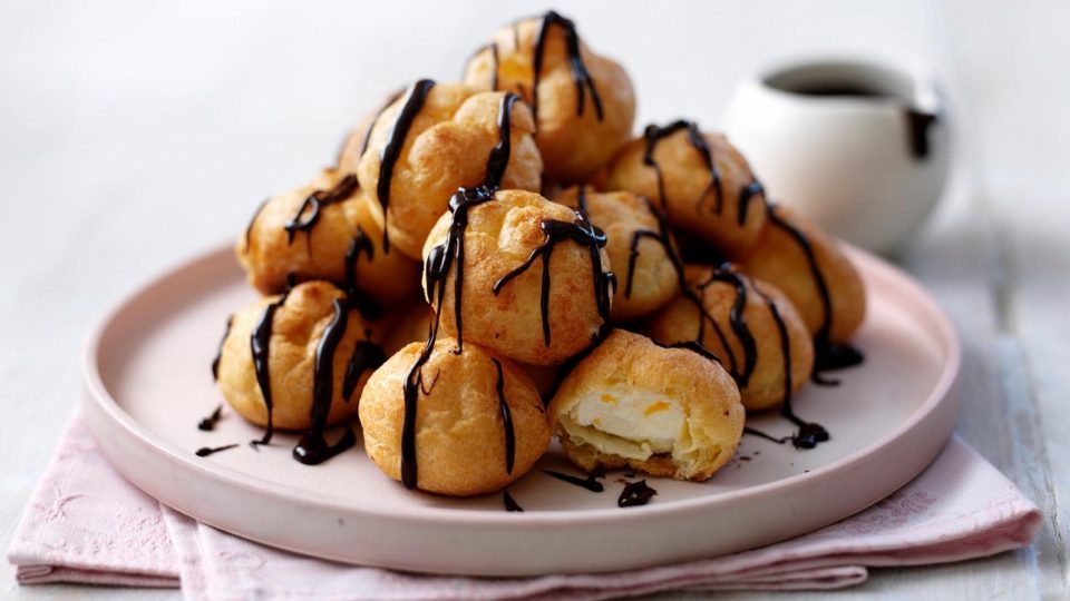 Torre de profiteroles con salsa de chocolate sobre un plato claro.