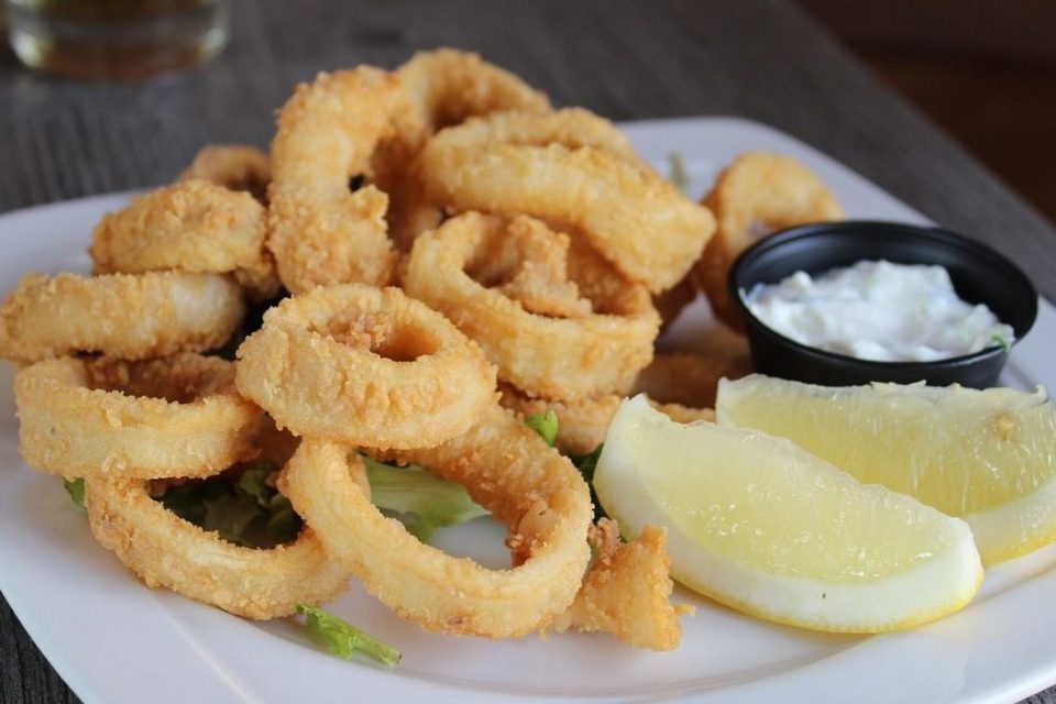 Calamares fritos acompañados de rodajas de limón y salsa blanca.