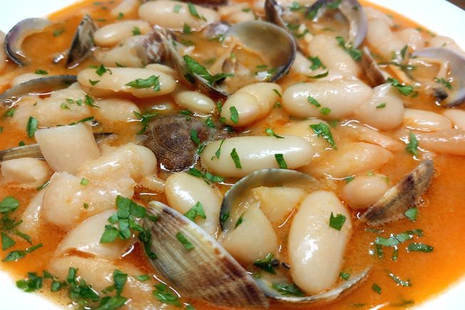 Plato de almejas y judías blancas en salsa con perejil.