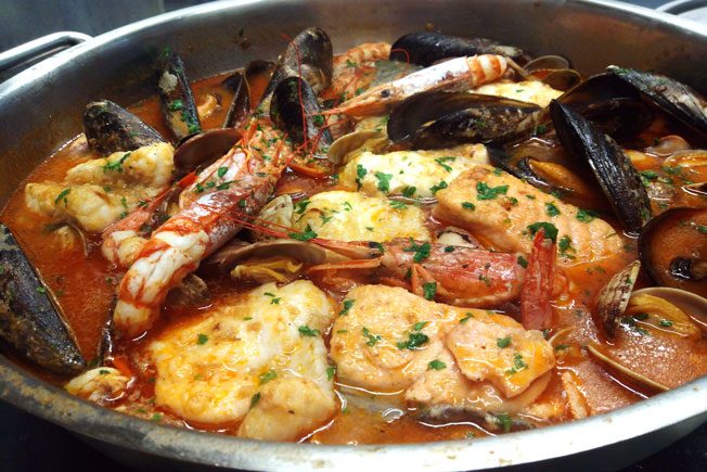 Plato de mariscos con pescado, mejillones, camarones y salsa roja. Decorado con perejil.