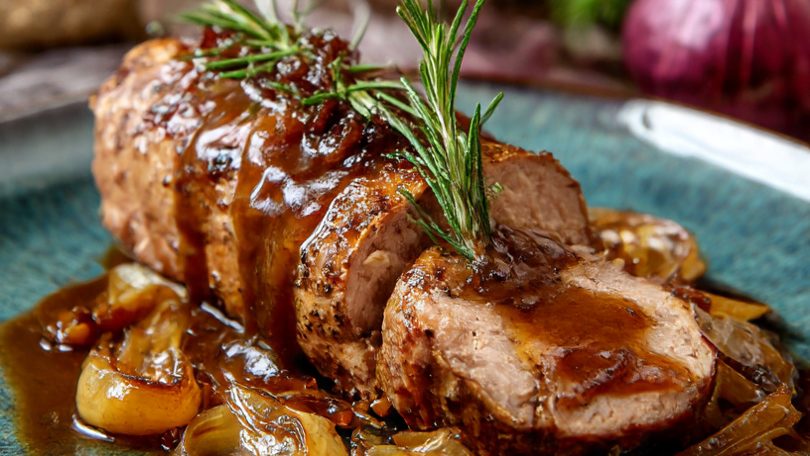 Solomillo de carne asada al pedro ximenez con salsa y hierbas, acompañado de guarnición vegetal.