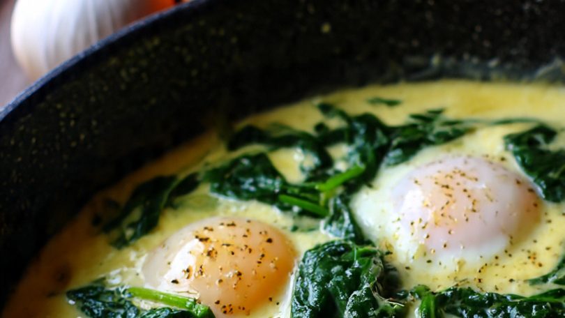 Dos huevos escalfados sobre espinacas en una sartén con mezcla de huevo y especias.