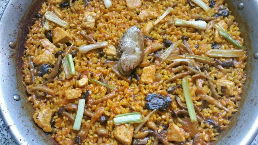 Paella con pollo, mariscos, verduras y especias en un plato grande.