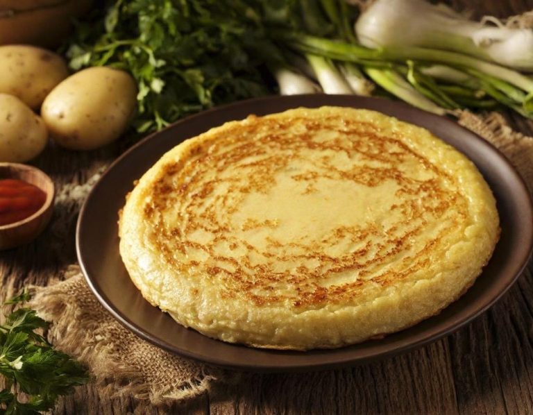 Tortilla española dorada, acompañada de patatas, cebollas y salsa roja en un plato.