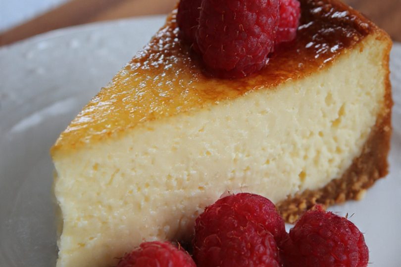 Tarta de queso con una capa dorada y frambuesas frescas en el lado.