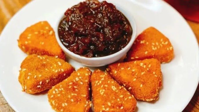 Siete nuggets de pollo empanizados con salsa oscura en un plato blanco.