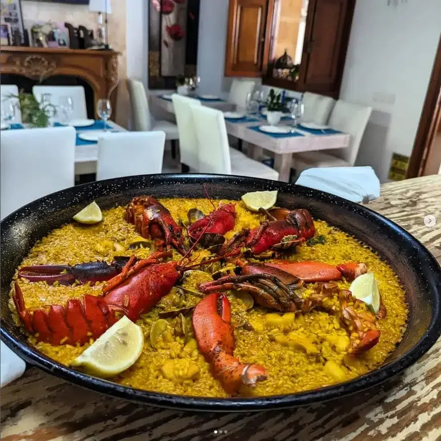 paella bogavante con mariscos, decorada con limón, servida en un recipiente negro.